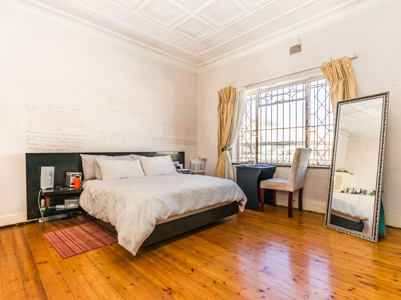 Spacious bedroom featuring original pressed metal ceilings and polished timber flooring, requiring cosmetic updates to walls and window fixtures.