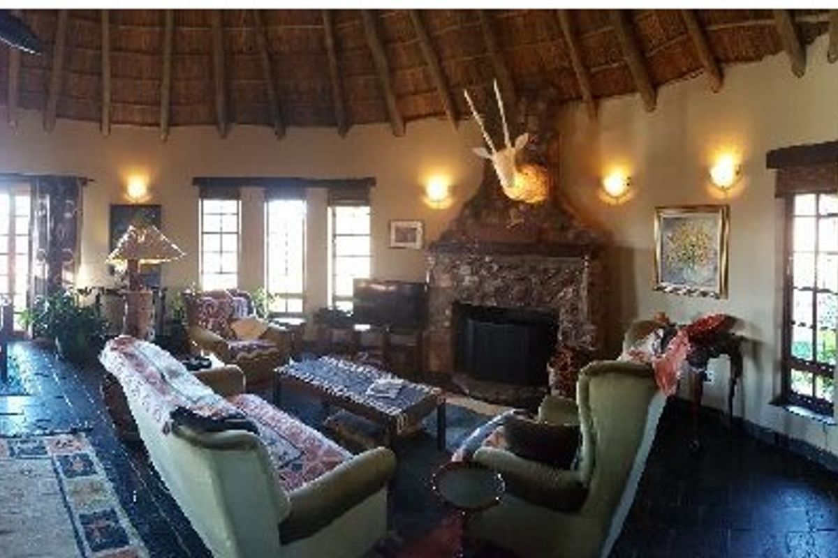 Spacious living room featuring a traditional thatched roof, stone fireplace, and dark slate flooring, creating a rustic and warm atmosphere.