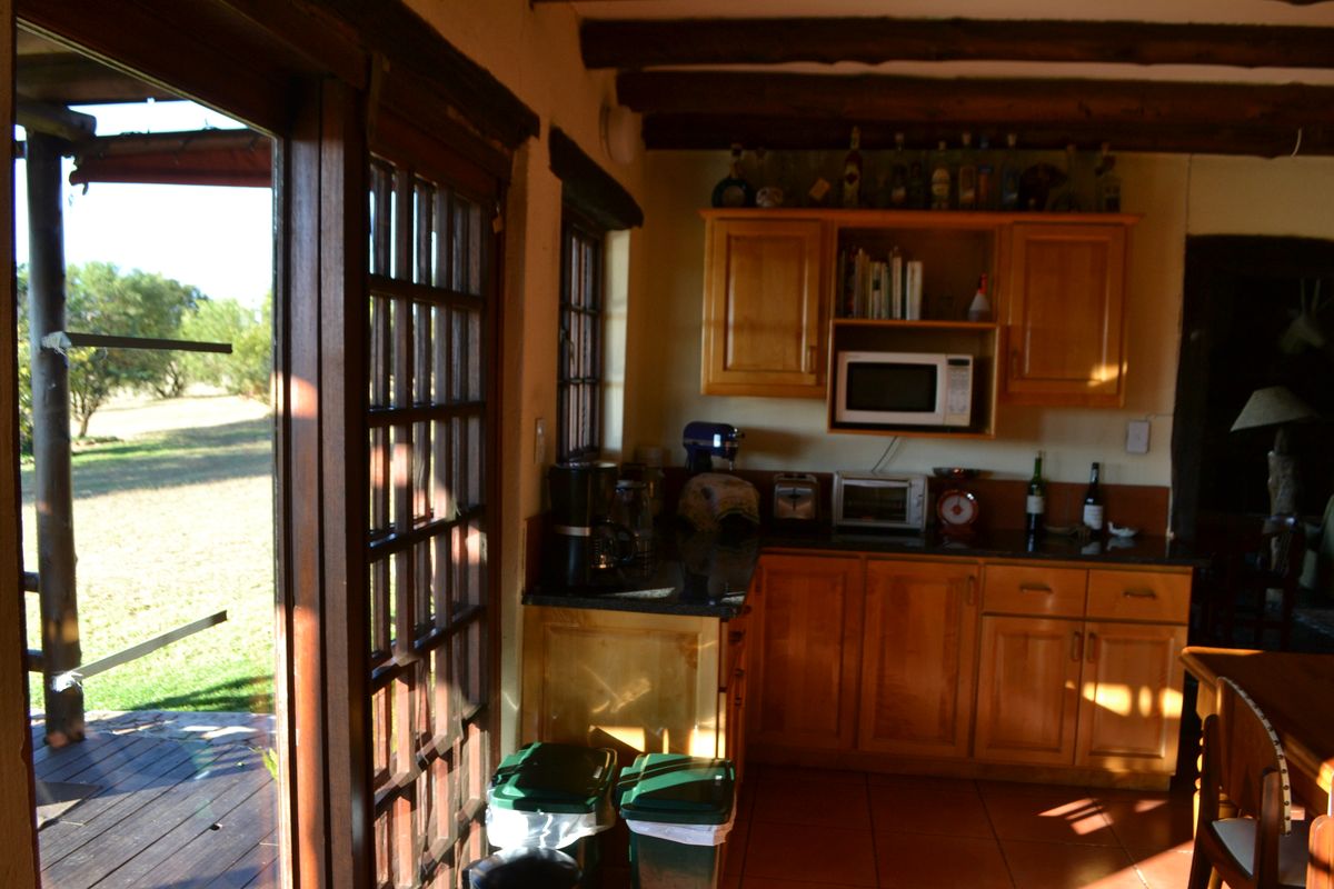A rustic kitchen featuring wooden cabinetry, granite countertops, and exposed timber ceiling beams, with direct access to an outdoor patio area.