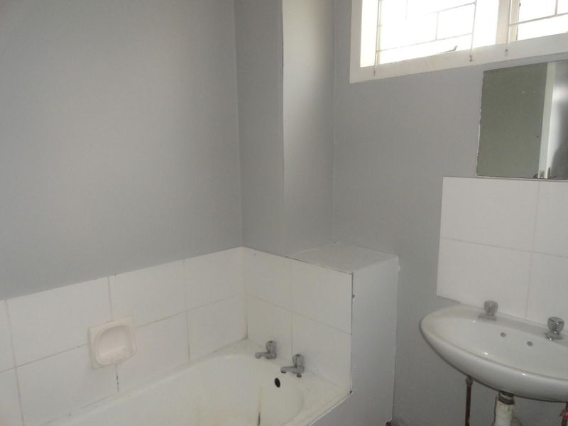 A functional bathroom featuring a bathtub, pedestal basin, and tiled splashbacks, requiring cosmetic updates to improve its overall condition and appeal.