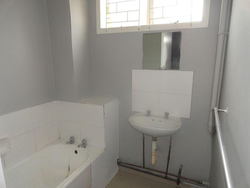 A functional bathroom featuring a built-in bathtub, pedestal washbasin, and tiled splashbacks. The space is ready for modernization and cosmetic updates.