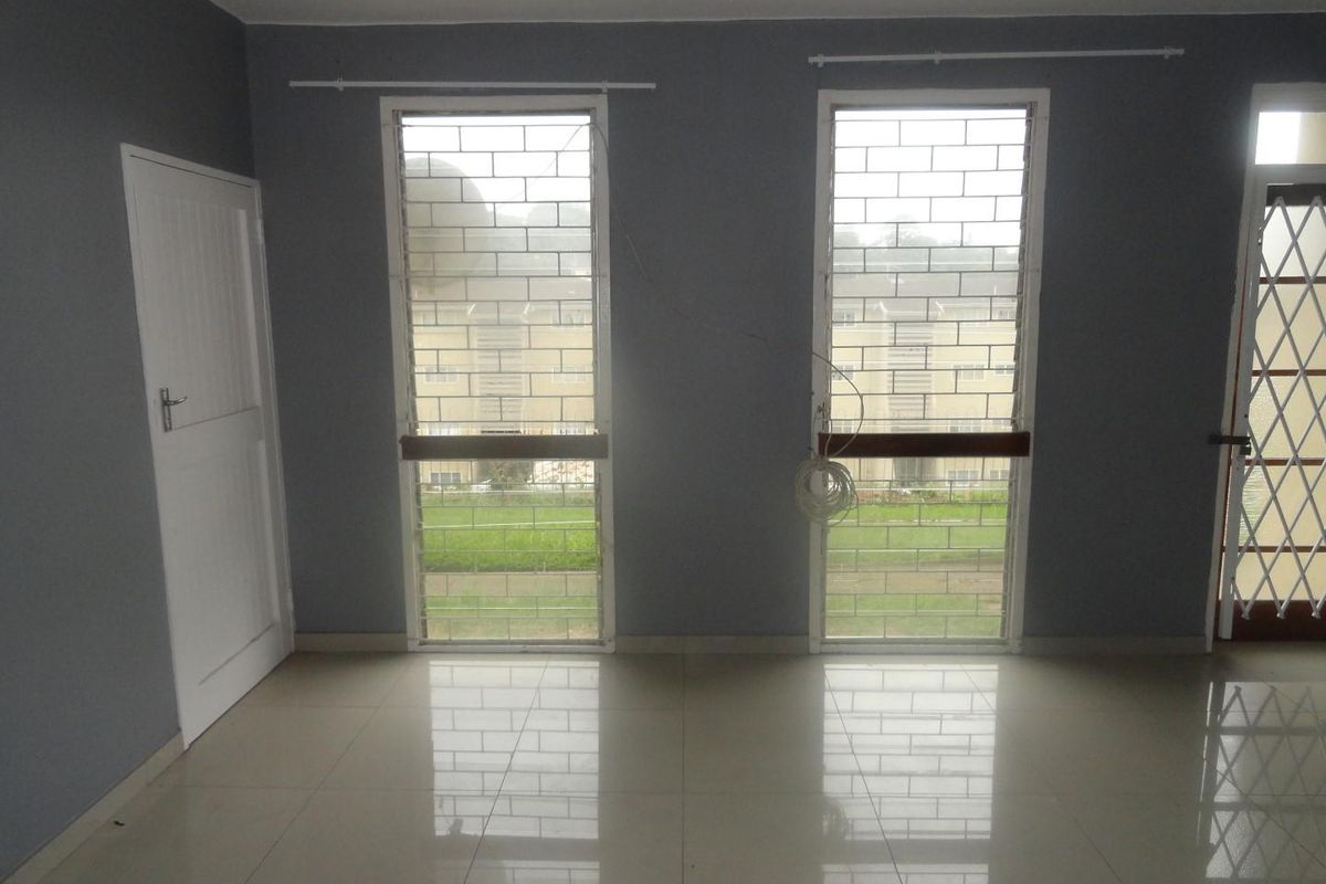 An empty living room featuring tiled flooring, security bars on the windows, and a security gate, providing a blank canvas for personalization.