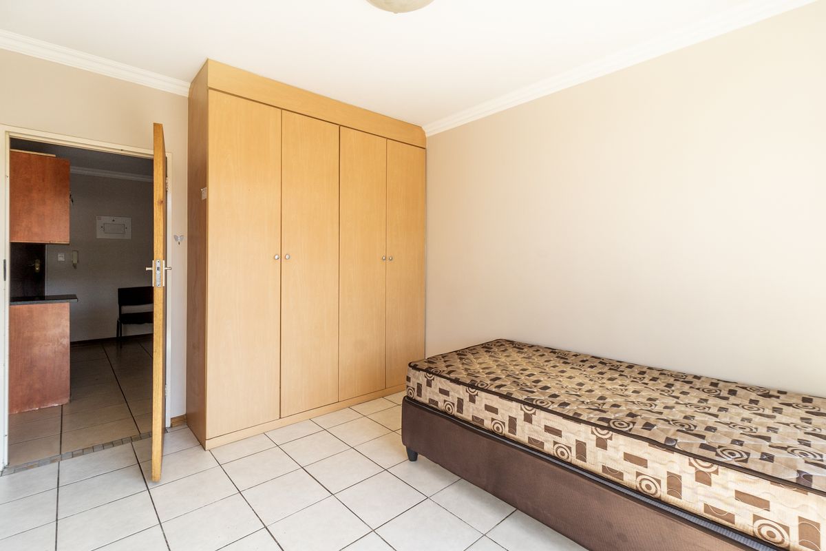A bedroom featuring light wood built-in wardrobes, tiled flooring, and decorative coving, with an adjacent view into a kitchen area.