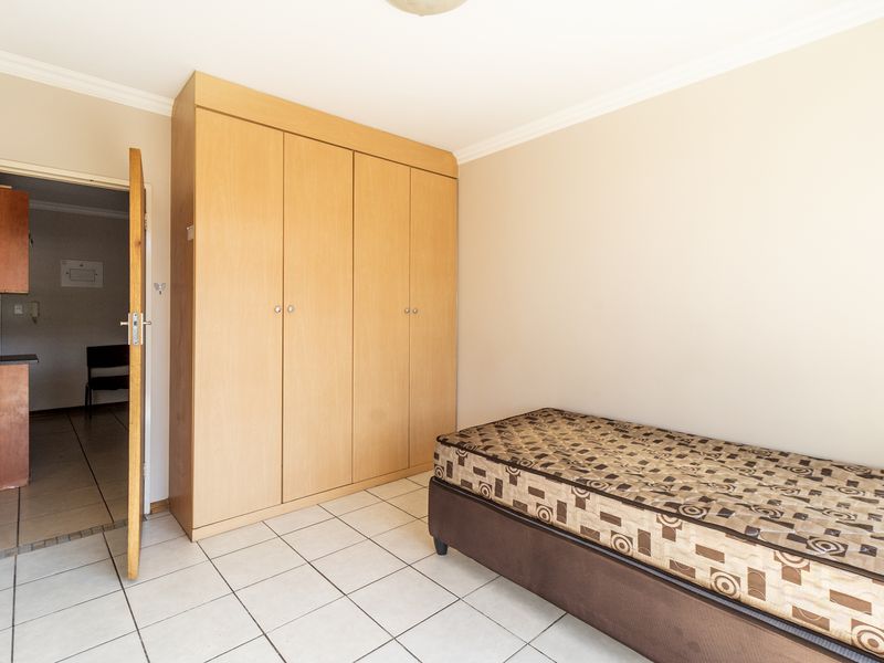 A bedroom featuring light wood built-in wardrobes, tiled flooring, and decorative coving, with an adjacent view into a kitchen area.