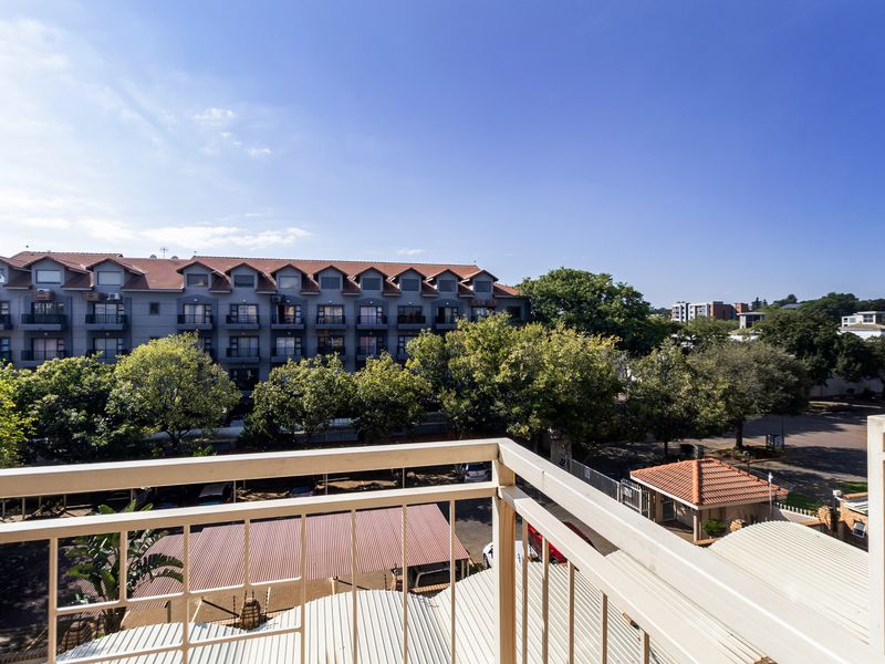 A balcony view overlooking the apartment complex grounds, featuring a metal balustrade and views of surrounding buildings and mature trees.