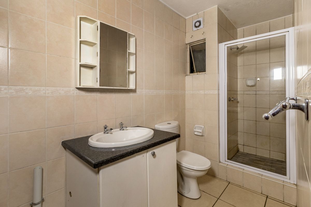 A functional bathroom featuring a vanity basin, toilet, and a glass-enclosed shower with neutral wall and floor tiling.