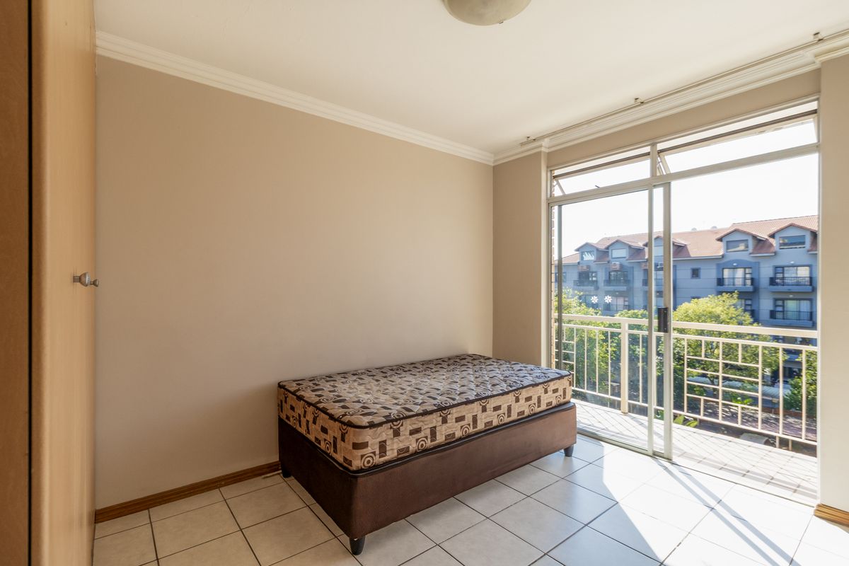A bedroom featuring tiled flooring, a built-in wardrobe, and a sliding glass door providing access to a balcony with an urban view.