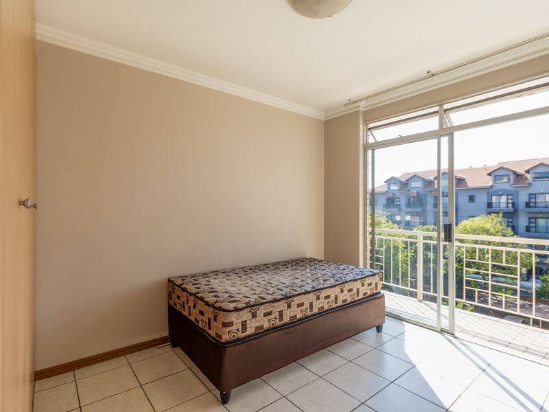 A bedroom featuring tiled flooring, a built-in wardrobe, and a sliding glass door providing access to a balcony with an urban view.