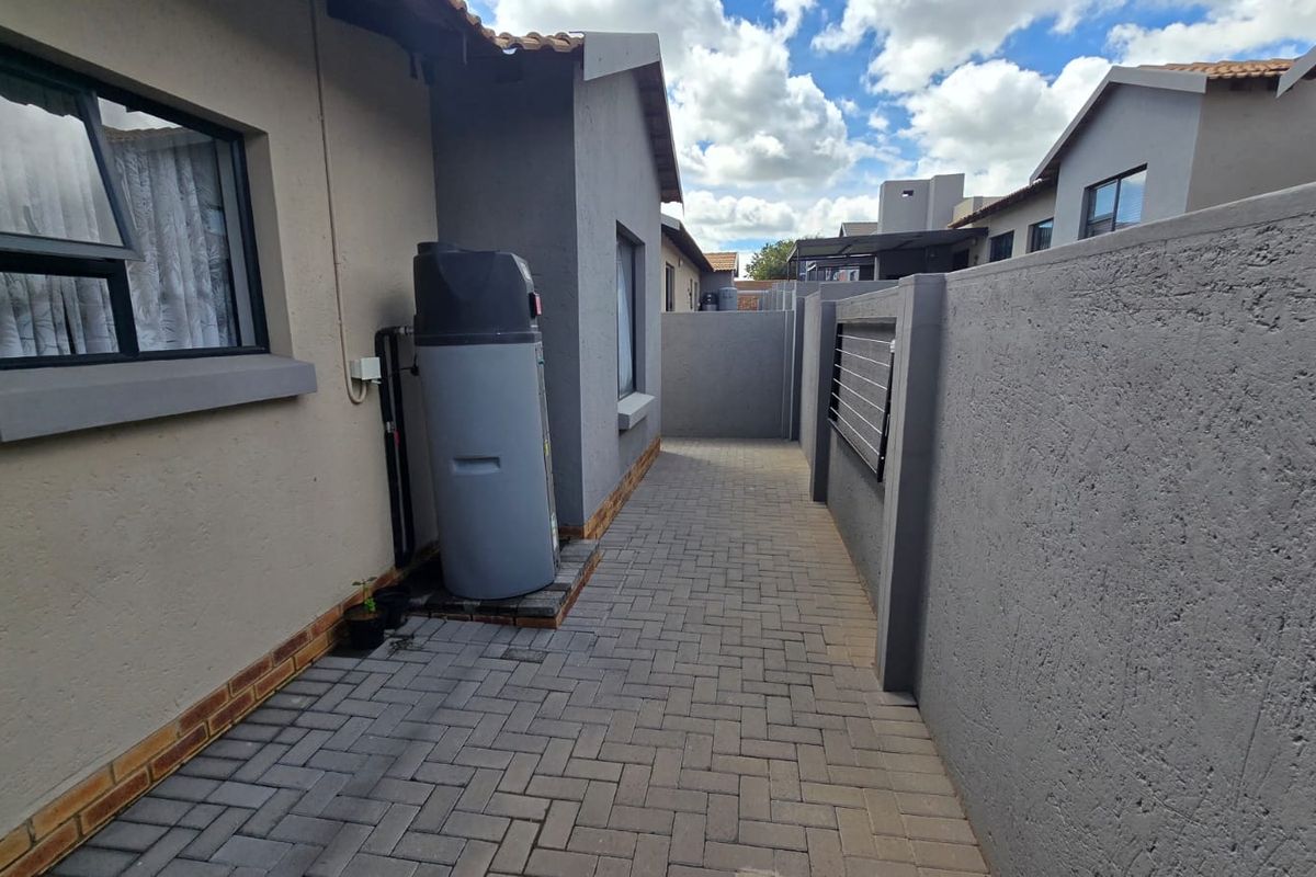 A paved side walkway of the townhouse featuring a boundary wall with electric fencing and an external geyser unit.