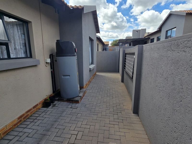 A paved side walkway of the townhouse featuring a boundary wall with electric fencing and an external geyser unit.