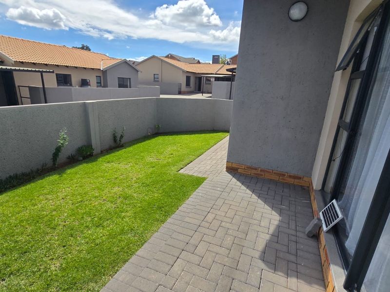 A private rear garden featuring a paved patio area and a well-maintained lawn, enclosed by a secure boundary wall.