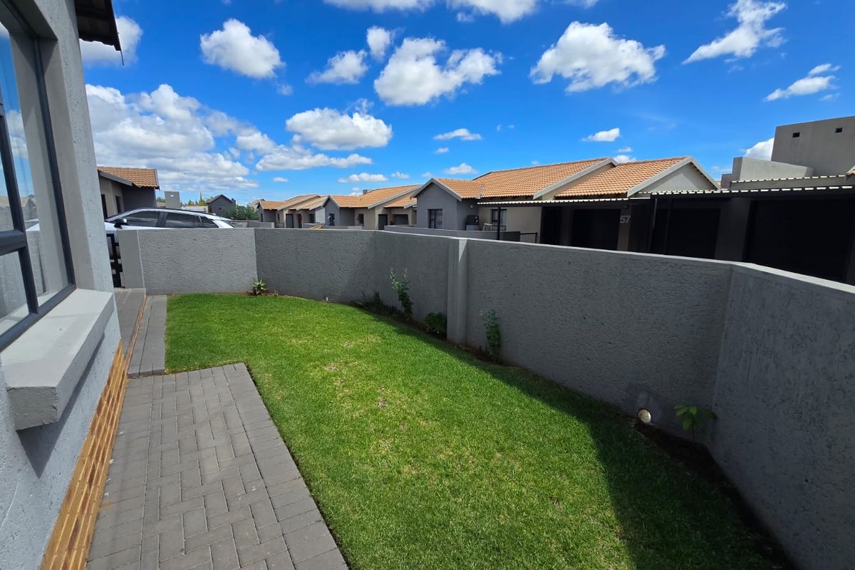 A private rear garden area featuring a paved walkway, a well-maintained lawn, and secure boundary walls within a townhouse complex.