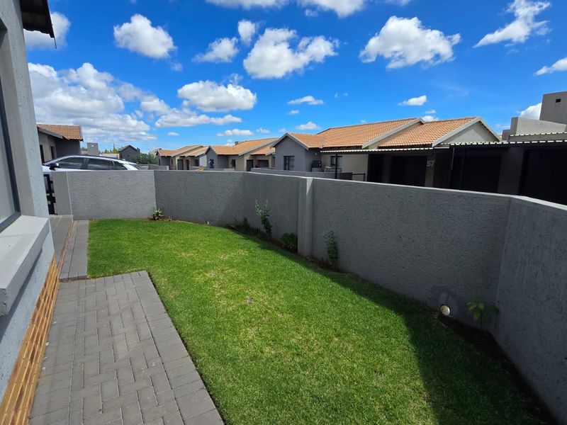 A private rear garden area featuring a paved walkway, a well-maintained lawn, and secure boundary walls within a townhouse complex.