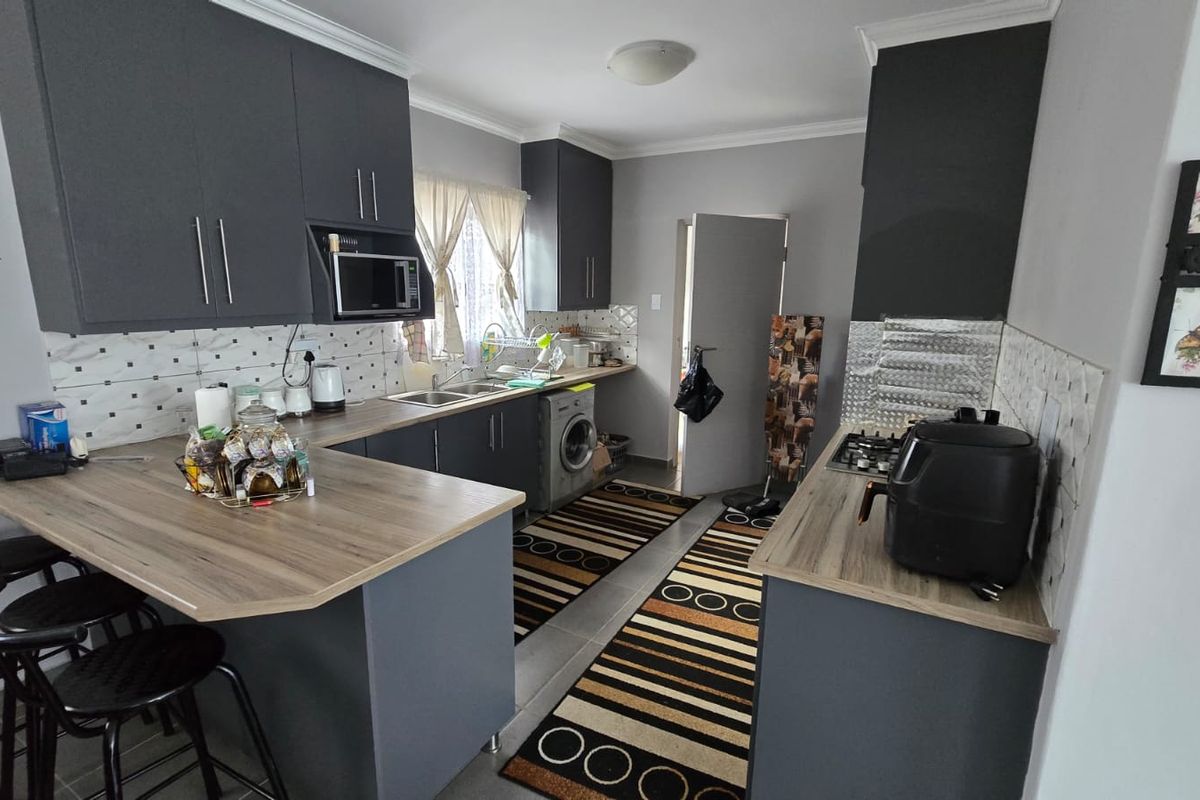 Modern kitchen featuring dark grey cabinetry, wood-look laminate countertops, a breakfast bar, and integrated gas hob with tiled backsplash.
