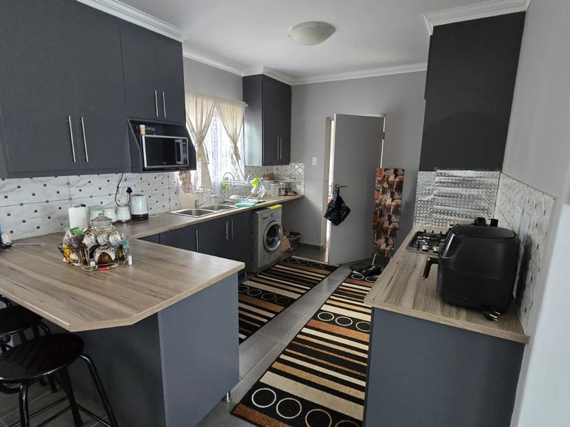 Modern kitchen featuring dark grey cabinetry, wood-look laminate countertops, a breakfast bar, and integrated gas hob with tiled backsplash.