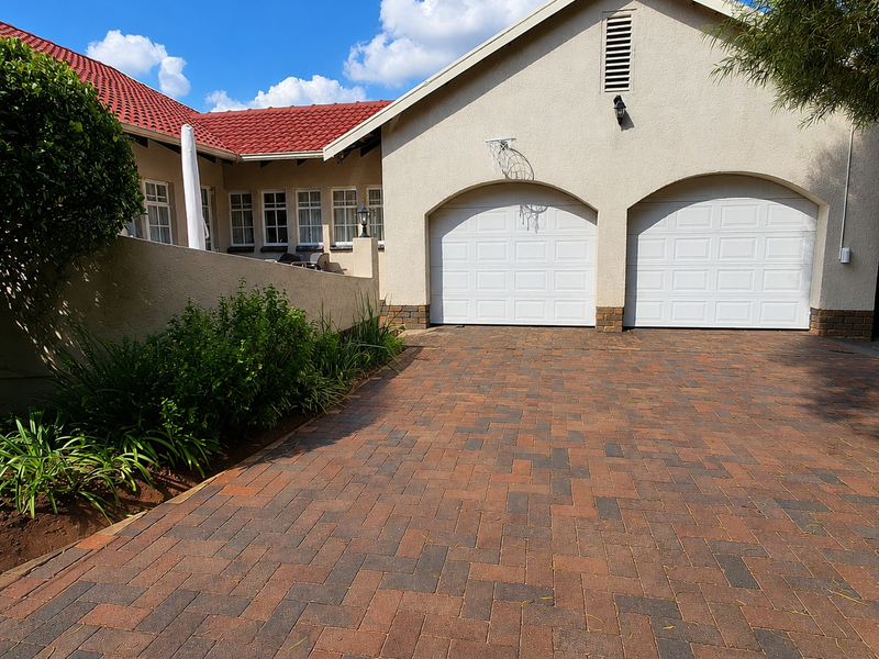 Front view of a well-maintained house featuring a double garage, paved driveway, and classic tiled roof architecture.