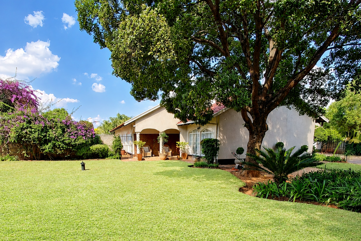 A well-maintained rear garden featuring a lush lawn, mature tree, and a covered patio area attached to the main house structure.