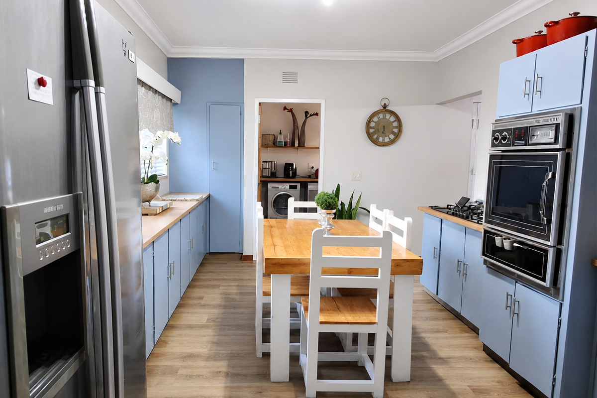 A well-maintained kitchen featuring light blue cabinetry, built-in oven and microwave, gas hob, and wood-look laminate flooring, with an adjacent laundry area visible.