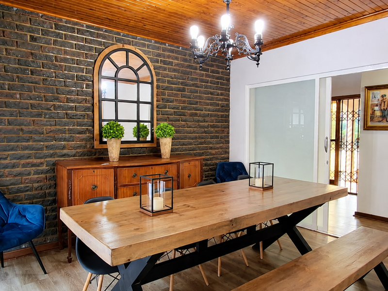 A well-maintained dining room featuring an exposed brick feature wall, warm timber ceiling, and a classic wrought iron chandelier.