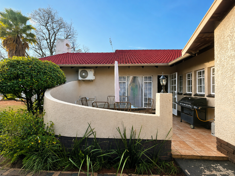 A covered patio area featuring tiled flooring, a curved masonry wall, and an exterior air conditioning unit, providing a functional outdoor space.