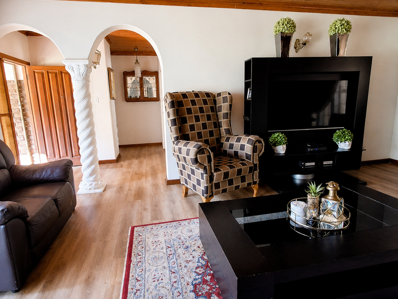 A living room featuring a warm timber ceiling, decorative column, and arched entryway, finished with modern laminate flooring.