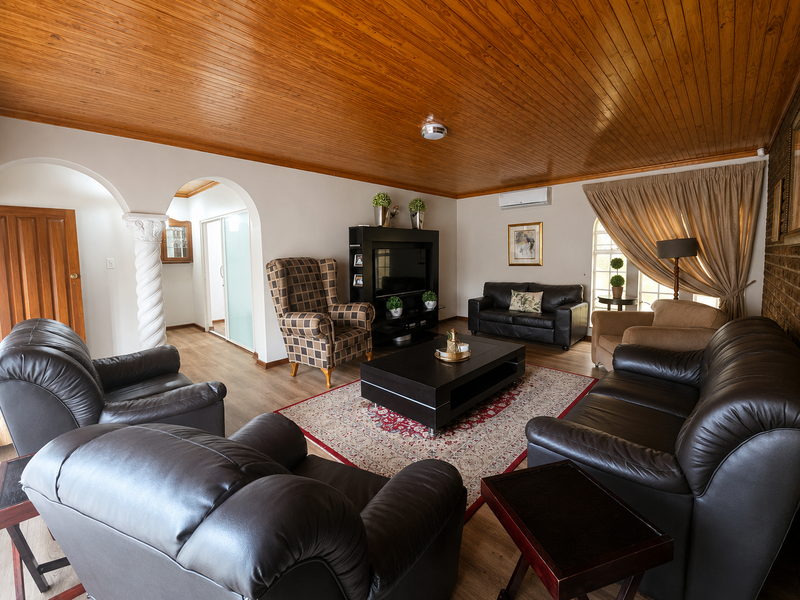 Spacious living room featuring a warm timber tongue and groove ceiling, decorative archways, and a brick feature wall with split system air conditioning.