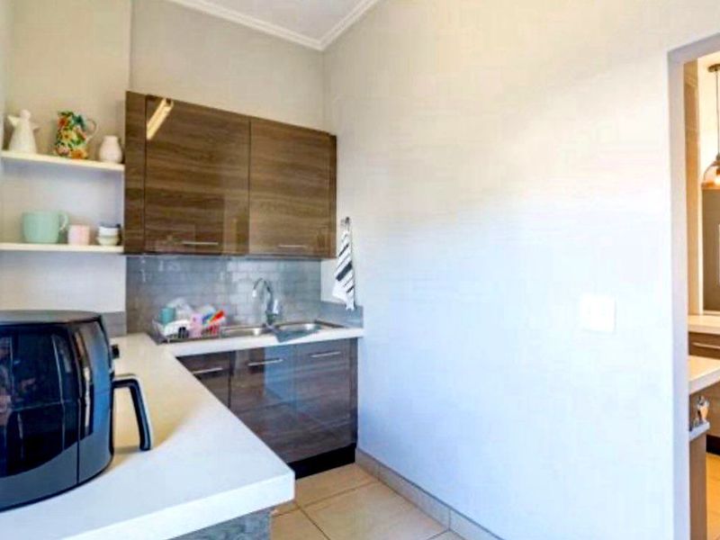 A functional scullery featuring modern wood-finish cabinetry, stone countertops, a stainless steel sink, and a clean subway tile backsplash.