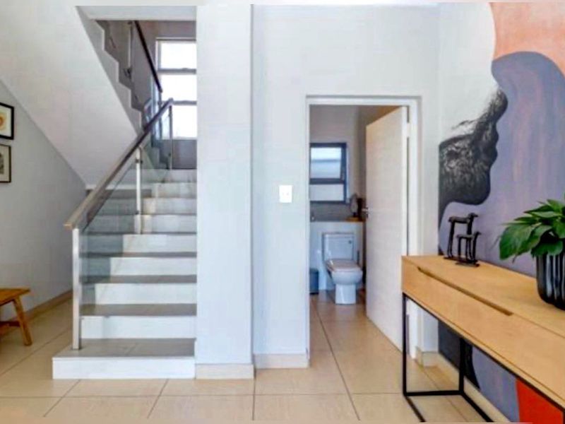 Modern entrance hall featuring a tiled staircase with a glass balustrade and direct access to a guest bathroom.