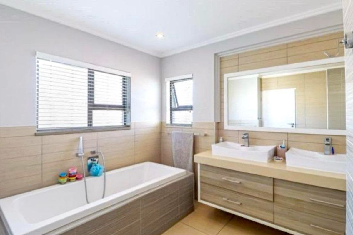 Modern bathroom featuring a double vanity with wood-finish cabinetry, a built-in bathtub, and neutral wall tiling.