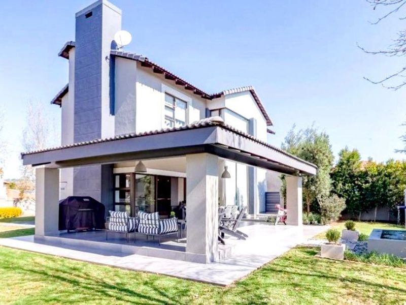 Rear view of the house featuring a spacious covered patio, tiled roof, and a landscaped garden with a built-in water feature.