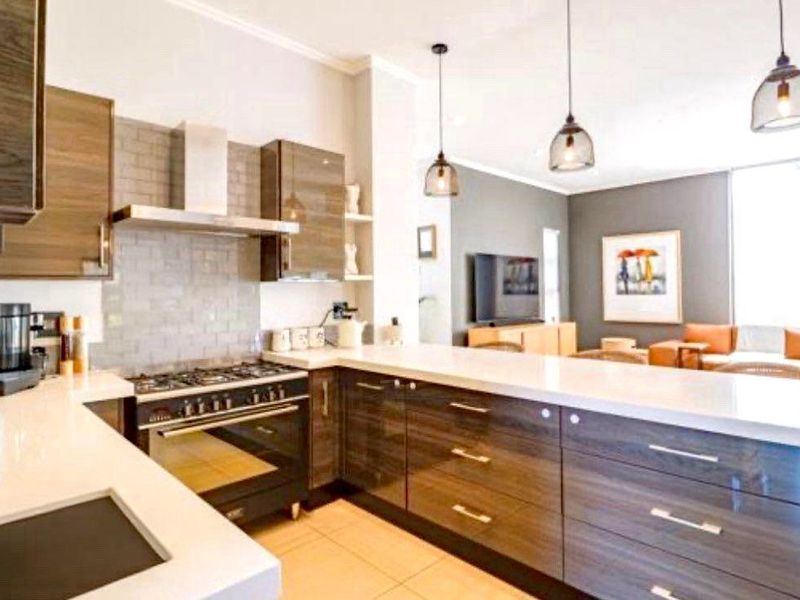 Modern open-plan kitchen featuring high-gloss cabinetry, quartz countertops, subway tile backsplash, and integrated gas stove, flowing into a comfortable living area.