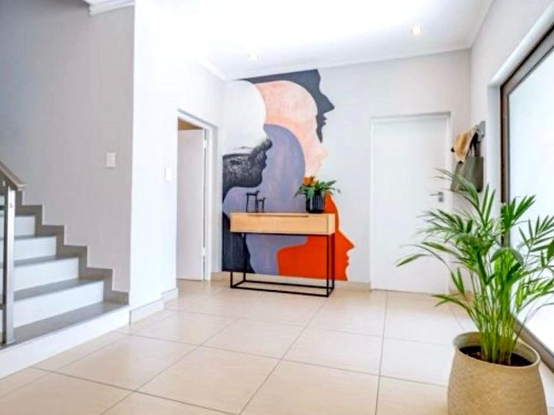 A bright and welcoming entrance hall featuring modern tiled flooring, a sleek staircase with a stainless steel balustrade, and recessed lighting.