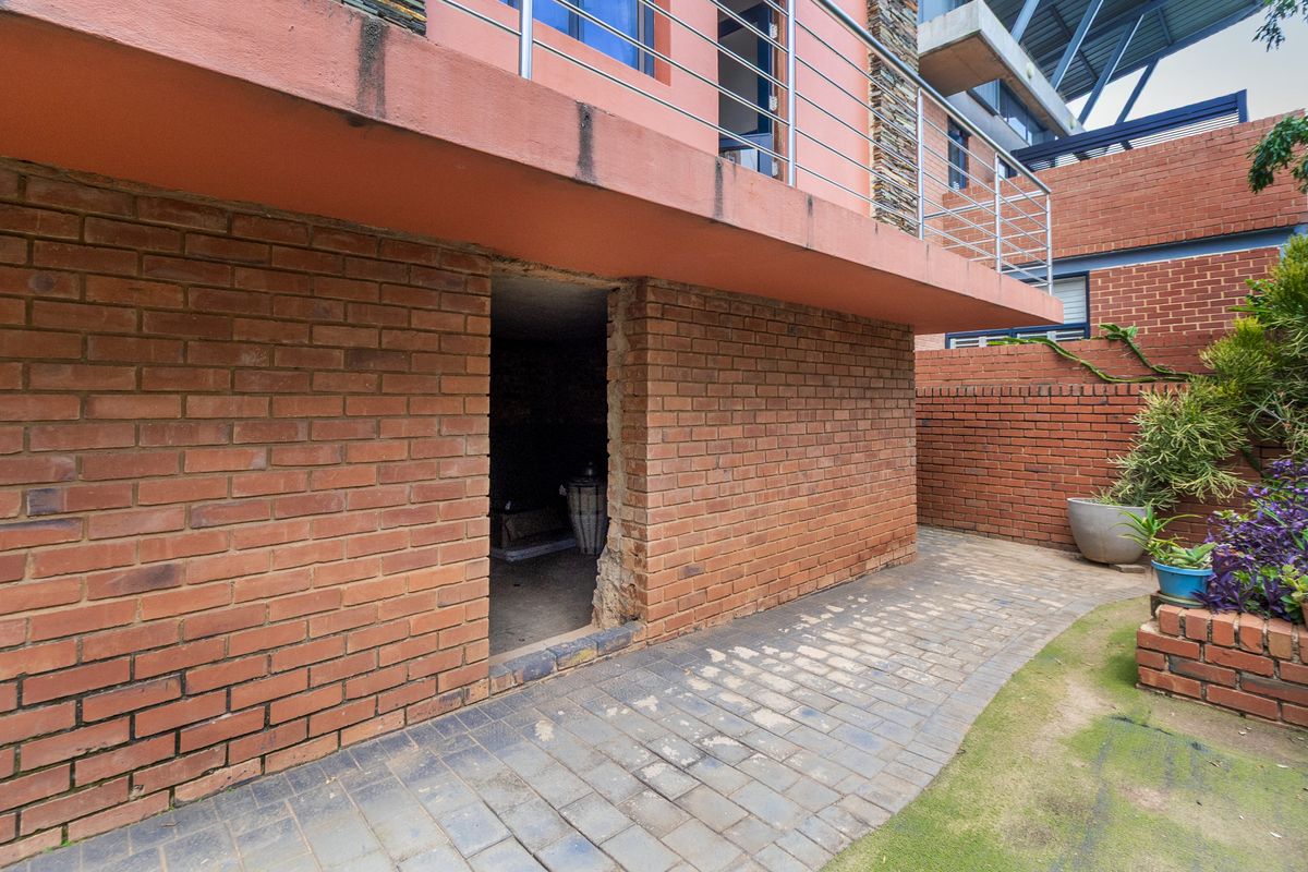 Rear exterior view showing a paved patio area, brick wall construction, and a balcony above with metal railings.