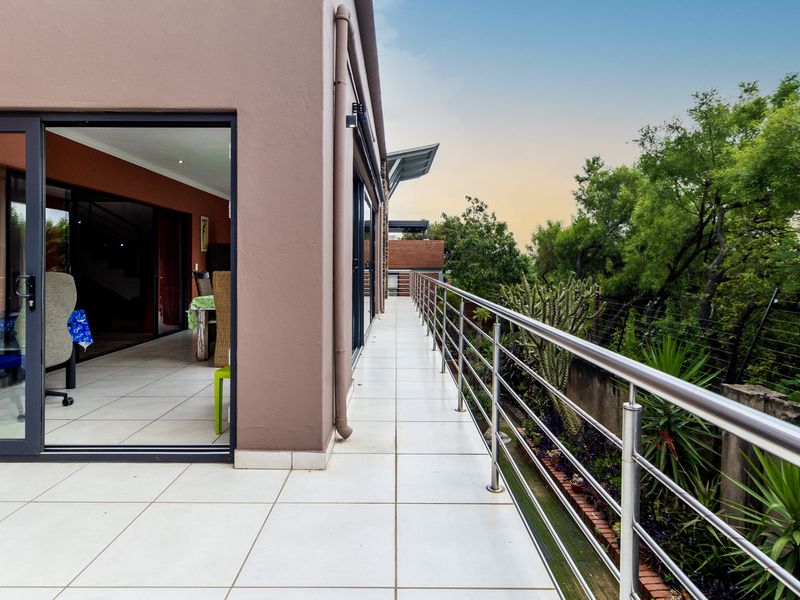 A spacious, tiled balcony featuring a modern stainless steel balustrade and large sliding glass doors providing seamless indoor-outdoor flow.