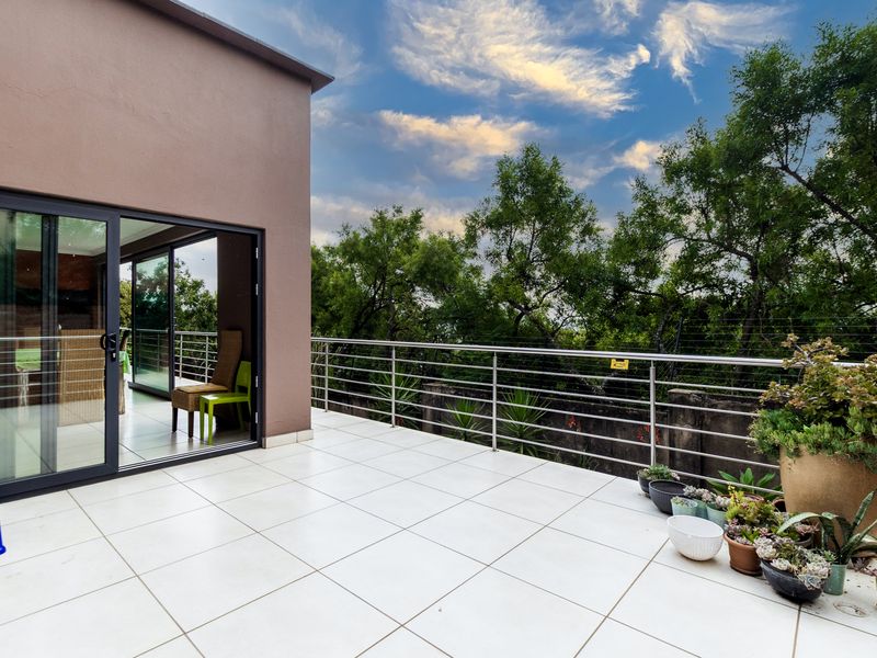 A spacious, tiled balcony featuring a modern stainless steel balustrade and large sliding glass doors providing seamless indoor-outdoor flow.
