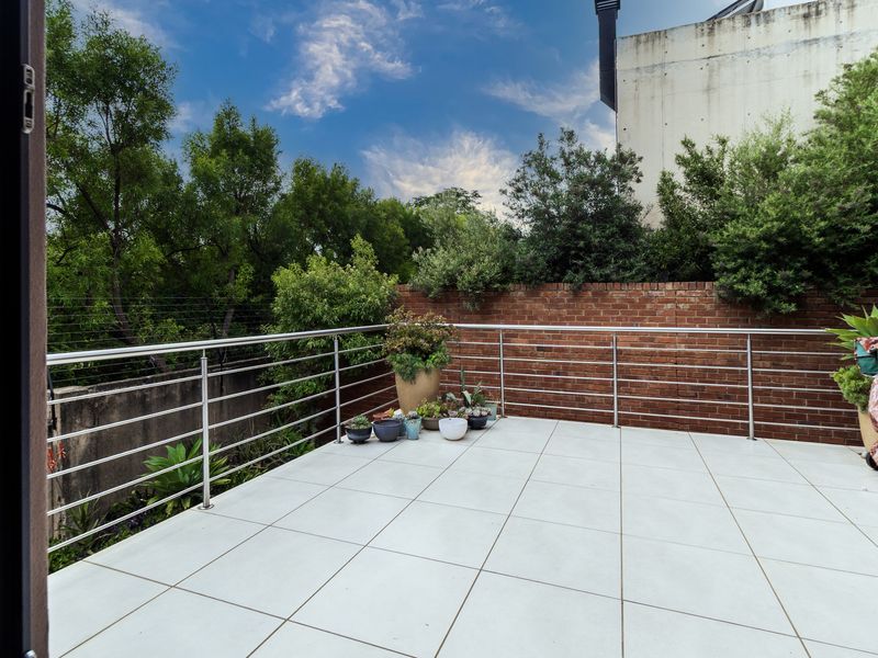 A spacious balcony featuring modern tiled flooring, a stainless steel balustrade, and a brick boundary wall with electric fencing.