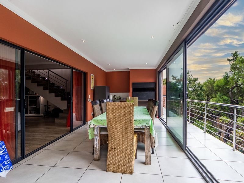 Covered patio featuring tiled flooring, a built-in braai, and large sliding glass doors opening to a balcony with stainless steel railings.