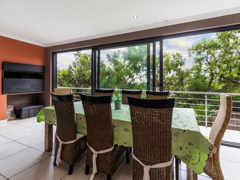 Dining area featuring a built-in braai, large sliding glass doors opening to a balcony, and tiled flooring with views of the surrounding trees.