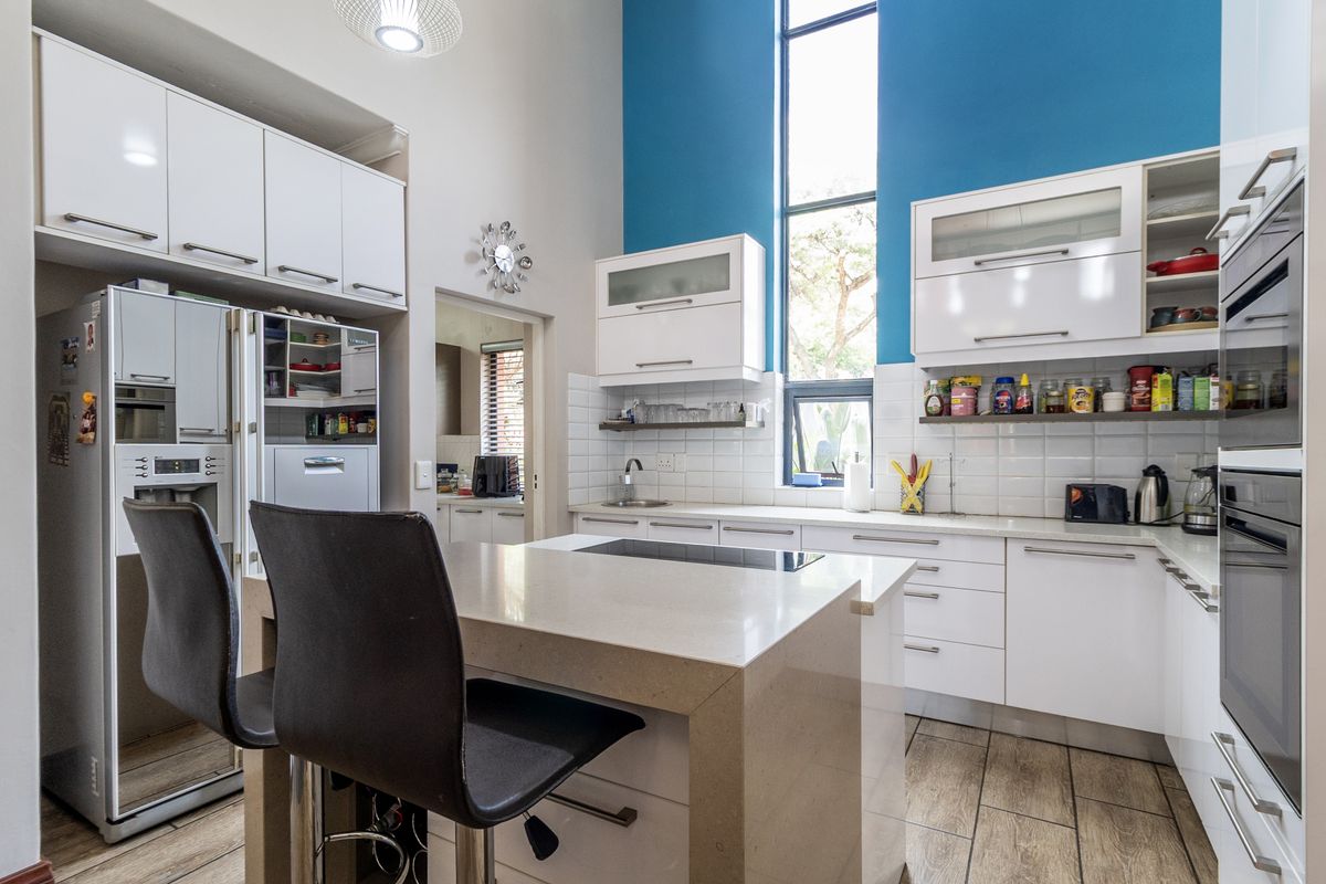 Modern kitchen featuring a central island with quartz countertops, built-in appliances, high ceilings, and a striking blue accent wall with a tall window.