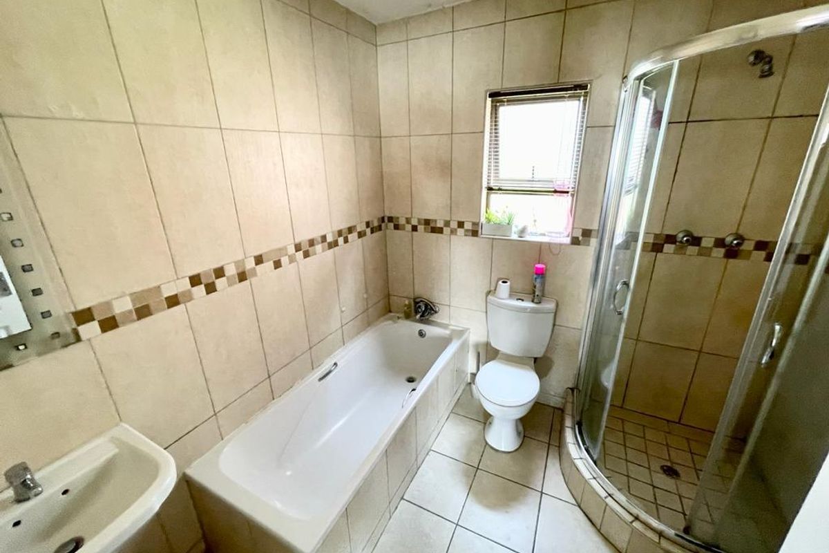 A functional bathroom featuring a built-in bathtub, separate glass-enclosed shower, pedestal basin, and toilet with neutral wall and floor tiling.