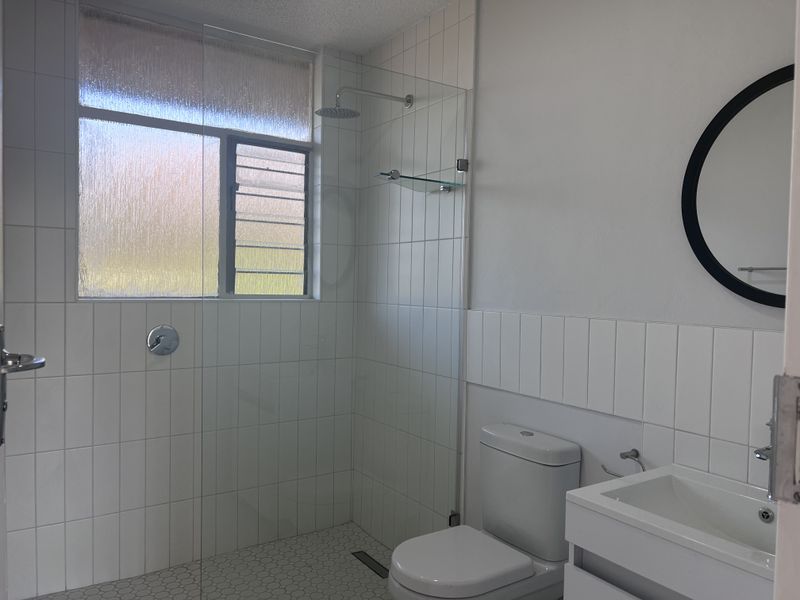 A clean, modern bathroom featuring a glass-enclosed walk-in shower, wall-mounted vanity, and white tiled finishes throughout.