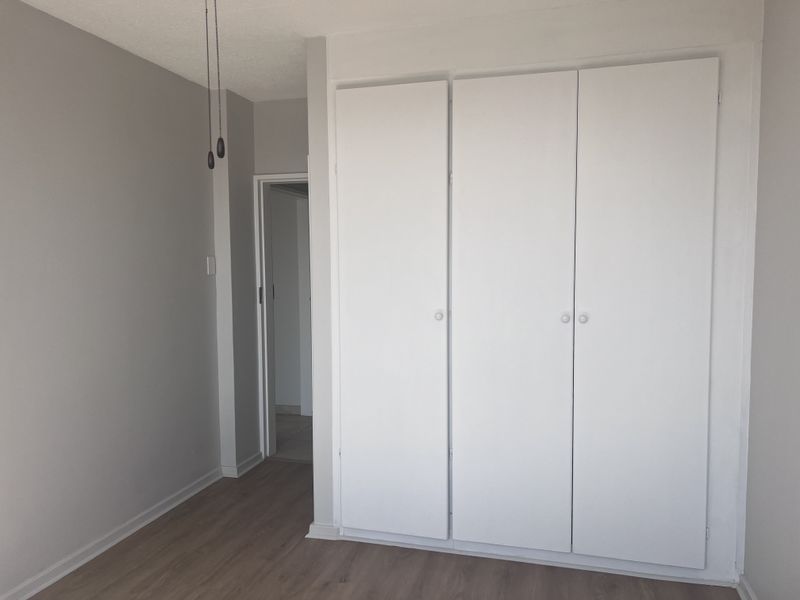 A clean, empty bedroom featuring neutral walls, laminate flooring, and a functional built-in wardrobe with white doors.
