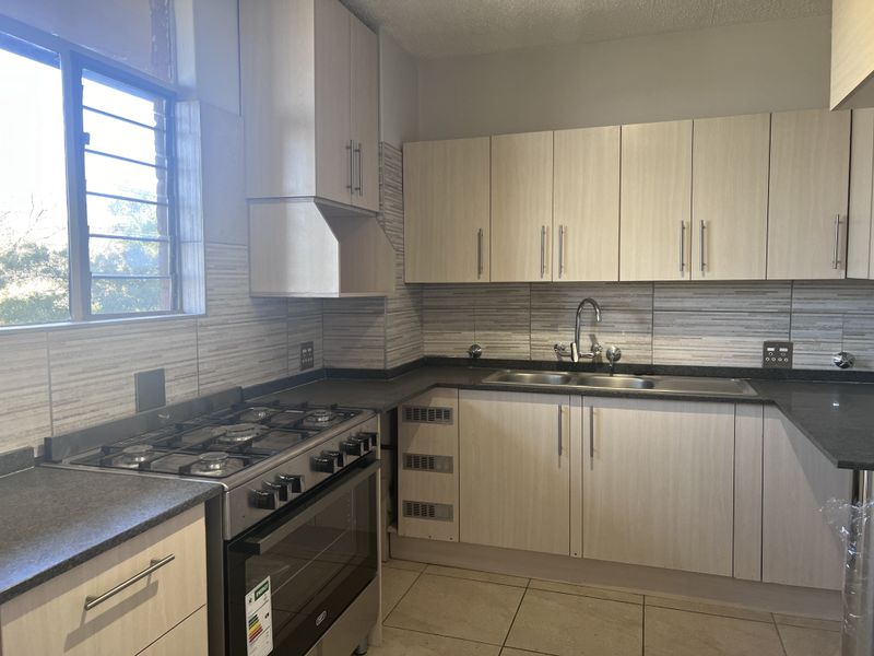 A functional kitchen featuring light wood-finish cabinetry, dark laminate countertops, a gas stove with oven, and tiled backsplash, ready for final finishing touches.