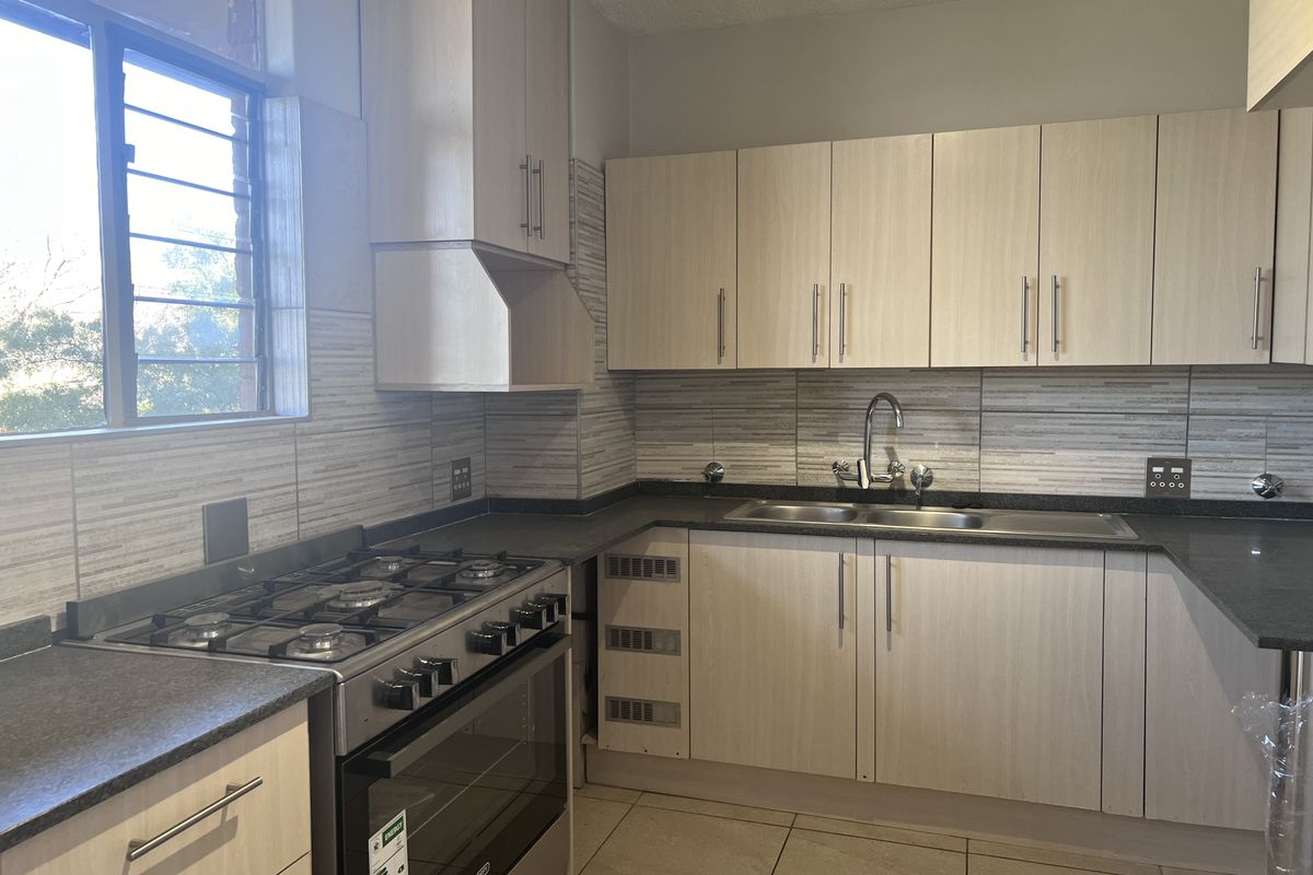 A functional kitchen featuring light wood-finish cabinetry, dark laminate countertops, a gas stove with oven, and tiled backsplash, ready for final finishing touches.