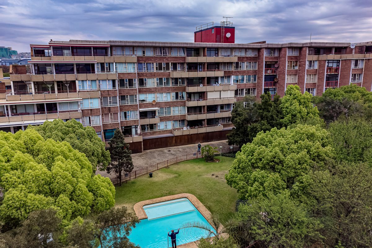 Aerial view of a multi-story residential townhouse complex featuring a communal swimming pool, landscaped garden areas, and paved driveway access.