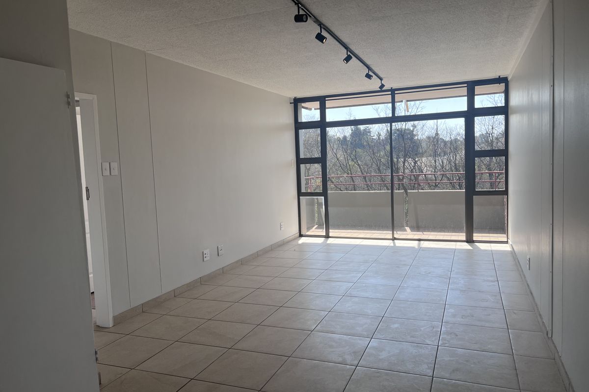 Spacious, empty living area featuring neutral tiled flooring, track lighting, and large sliding glass doors leading to a private balcony.