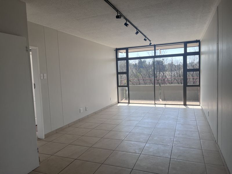 Spacious, empty living area featuring neutral tiled flooring, track lighting, and large sliding glass doors leading to a private balcony.