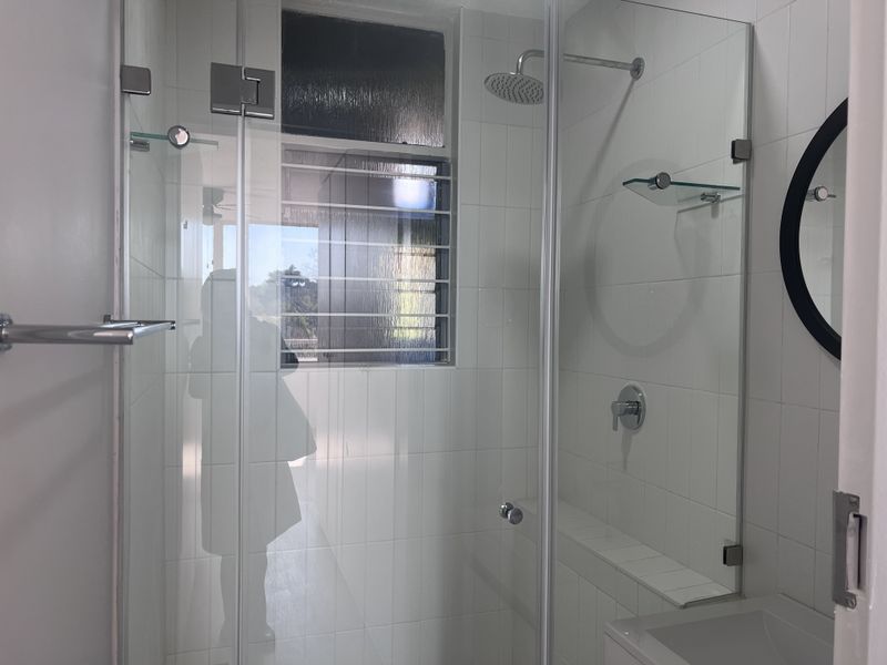 A clean, modern bathroom featuring a glass-enclosed shower with a rain shower head and white wall tiling.