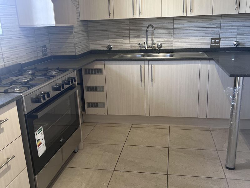 Modern kitchen featuring light wood-finish cabinetry, stone countertops, a gas stove with oven, and neutral tiled flooring.