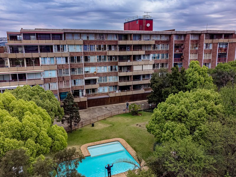 Aerial view of a multi-story residential townhouse complex featuring a communal swimming pool, landscaped garden areas, and paved driveway access.